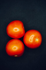 A trio of tomatoes on black background. Shallow focus, blur, red, 3, food prep, contrast, dark, lighting.