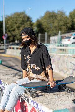 Mujer joven con mascarilla con skate monopatín en skatepark haciendo fotos selfies