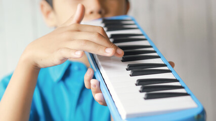 Boy playing blue melodeon musical instrument, melodica blow organ, pianica or melodion on blurry...