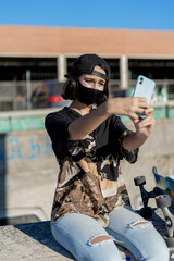 Mujer joven con mascarilla con skate monopatín en skatepark haciendo fotos selfies - obrazy, fototapety, plakaty