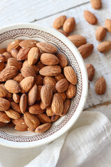 Almonds in a bowl on a white wooden table, flat lay style