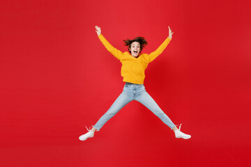 Full length of excited surprised cheerful young brunette woman 20s in basic yellow sweater jumping keeping mouth open spreading hands and legs isolated on bright red colour background studio portrait.