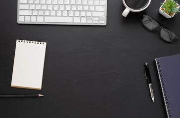 Top view above of Black leather office desk table with keyboard, notebook and coffee cup with equipment other office supplies. Business and finance concept. Workplace, Flat lay with blank copy space.