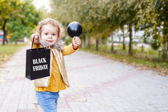 Smiling kid girl holding shopping bag on black friday and black inflatable ball outdoors