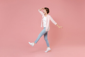 Full length side view of shocked young brunette woman 20s wearing casual checkered shirt holding hand at forehead looking far away distance isolated on pastel pink colour background, studio portrait.