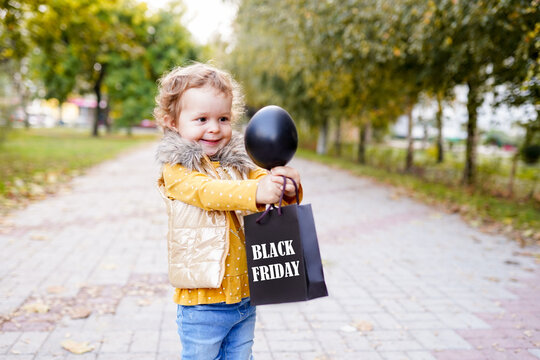 happy child holding shopping bag on black friday and black inflatable ball standing in the park