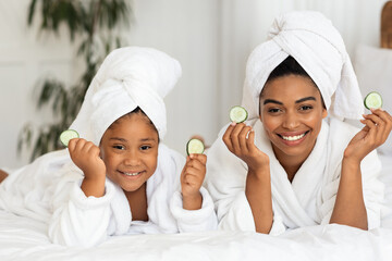 Beauty Time. African Mom And Daughter In Bathrobes Posing With Cucumber Slices