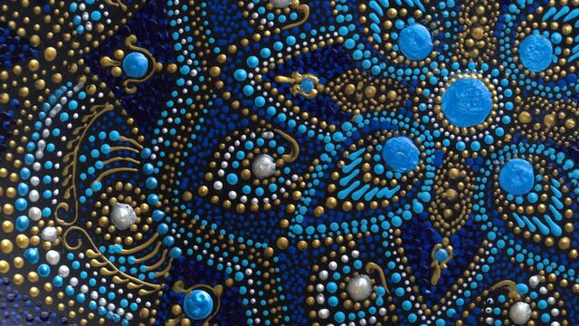 Decorative ceramic plate with black, blue and golden colors, painted plate rotating on background, closeup, top view. Decorative porcelain plate painted with acrylic paints, handwork, dot painting