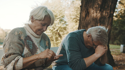 Elderly worried couple sitting on the bench in despair. Woman counting last coins. High quality...