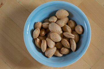 Almonds on table in hard nutshells, group of dry ripened fruits in blue bowl, crop food ingredients ready for cooking