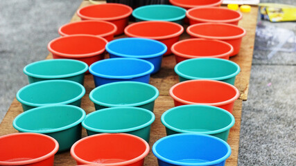 Selling Colorful tubs lined together on a wooden platform. Small plastic tubs filled with soap solution for blowing bubbles.