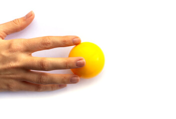 Fingers of a female hand touching a yellow plastic ball on a white background.