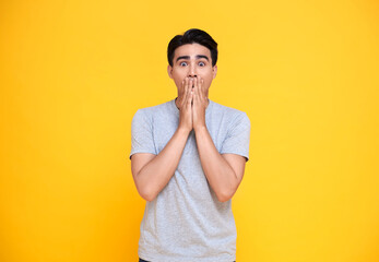Surprised and Shocked asian man covering mouth with hands isolated on bright yellow background.