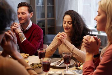 Multi-ethnic group of adult people praying at Thanksgiving dinner with friends and family