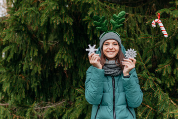 Christmas tree fir branches. Young woman holds snowflakes. Decorative antlers on had. Christmas decorations, candy canes and balls.