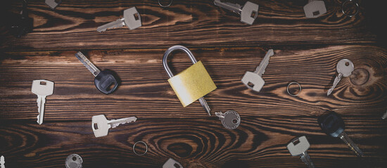 Studio photo of a lock with a broken key in it on a wooden background. Lots of other new keys around the lock.