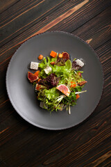 Mix of salads for the holiday Halloween, with pumpkin, figs, cheese and nuts, on a plate, on a wooden background
