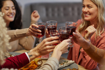 Close up of cheerful young people clinking glasses while sitting at table together and enjoying Thanksgiving dinner with friends and family, copy space