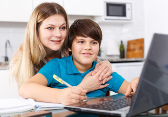 Woman helping tweenage boy with lessons sitting together at home kitchen