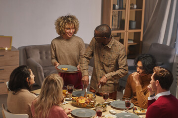 ortrait of smiling African-American man cutting roasted turkey while enjoying Thanksgiving dinner with friends and family, copy space