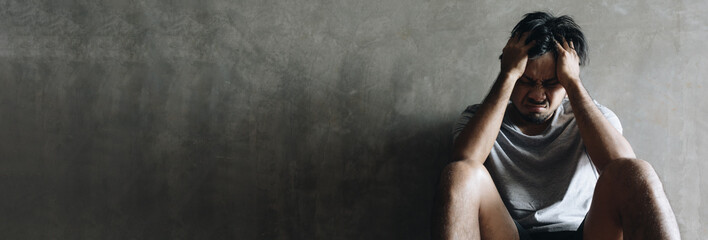 A depressed and strain young asian man sitting alone in the dark on grey wall with copy space, Life problems