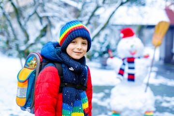 Happy kid boy with glasses having fun with snow on way to school, elementary class