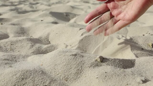 A woman's hand pouring sand through her fingers on a sandy beach