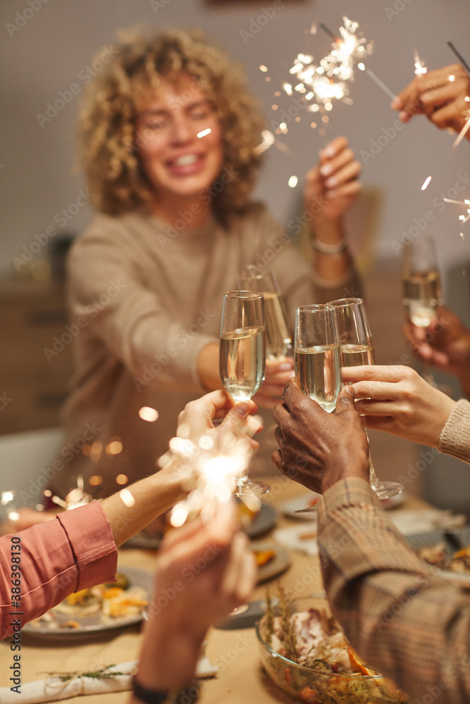 Wall mural Vertical close up of people toasting with champagne glasses while enjoying dinner party with friends and family and holding sparklers