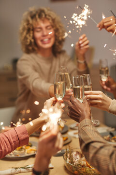 Vertical close up of people toasting with champagne glasses while enjoying dinner party with friends and family and holding sparklers