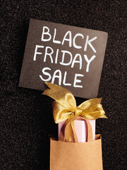 black board with chalk inscription "black friday sale" and gift-box in craft package on a black glitter background