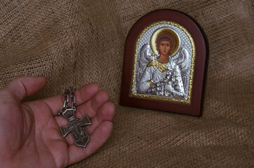 Christian orthodox icon of the Archangel Michael and a hand with a silver cross.