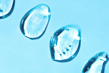 Transparent hyaluronic acid gel drops on a blue background.