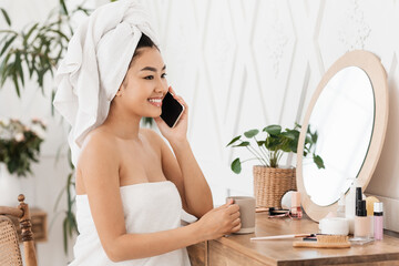 Happy asian woman talking on phone, sitting next to mirror