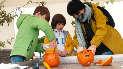 Mom and children make outdoor pumpkin decorations as a weekend activity in the fall. Face masks to protect against possible spread of infection. 