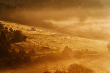 View of beautiful gold fog in the morning. Campervan on the meadow surounded by the forest. Sunrise landscape.