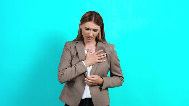 Depressed young woman, worried in business suit, who feels chest pain trying to breathe, heart problems, risk of heart attack, emergency. Studio image indoors, isolated on blue background