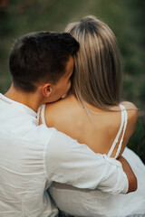 Fototapeta premium Young romantic couple is enjoying beautiful time together sitting on the green grass and hugging. Close up. Back view.