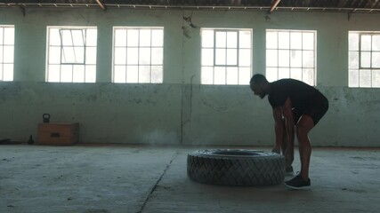 Strong man doing tire flip workout. Sportsman tossing a tyre during an intense workout session in an empty warehouse.
