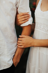 Love and romance. Close up of hands of couple in white clothes holding hands.