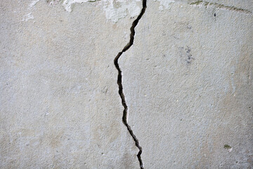 Huge crack divided grey concrete wall of the house. Close up. The destruction of buildings, violations of the construction.