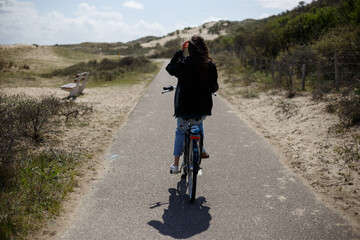 Fototapeta premium Full length view. Back view of a young girl walks single on bicycle on the road in sunny day time.