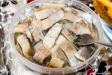 Sliced herring in oil, which is in a plastic jar with a fork.