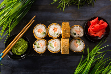 Set of baked sushi rolls with wasabi and ginger on black