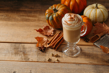 Spice pumpkin latte with cream foam, cinnamon stick, leaf and orange pumpkins