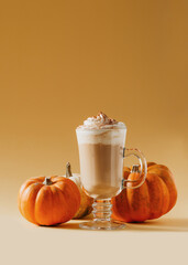 Spice pumpkin latte in glass with pumpkins on yellow background