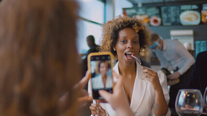 Back view of woman taking photo of african friend dining together at restaurant
