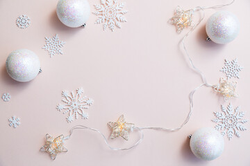Composition with white Christmas balls, garlands of lights and snowflakes on a light pink background copy space. Christmas and New Year concept