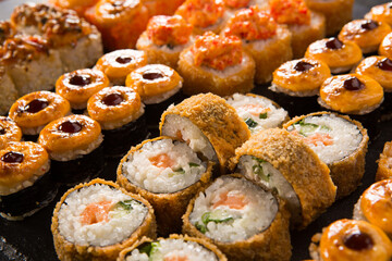 Set of baked sushi rolls with wasabi and ginger on black