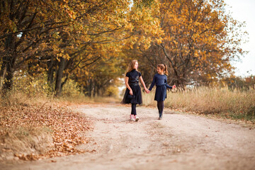 Obraz premium Two teenage girls walk along a forest road in the warm autumn.