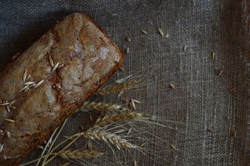 Homemade bread on a background of coarse burlap and spikelets of wheat, top view of a crispy crust